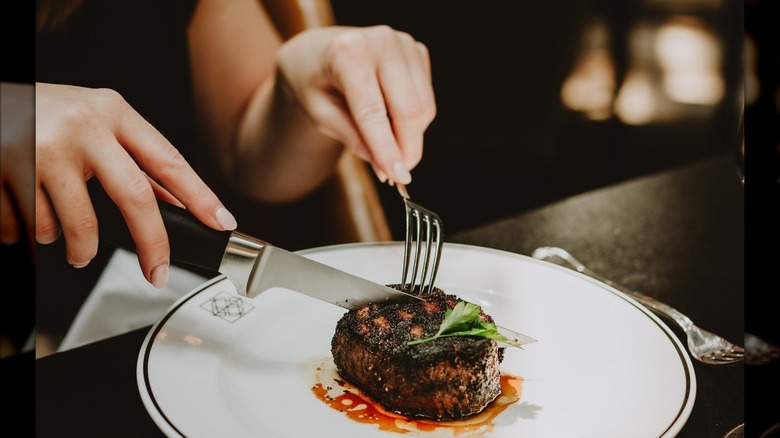 Hands holding knife and forl and cutting filet on white plate