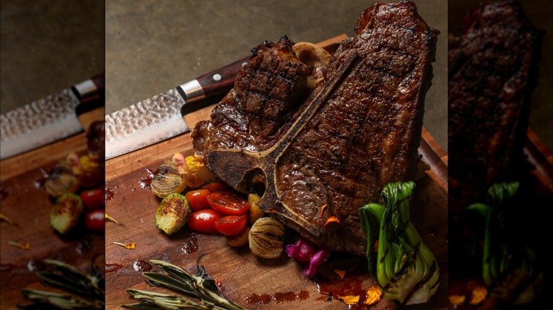 Steak with assortment of roasted veg and chef's knife on wooden cutting board