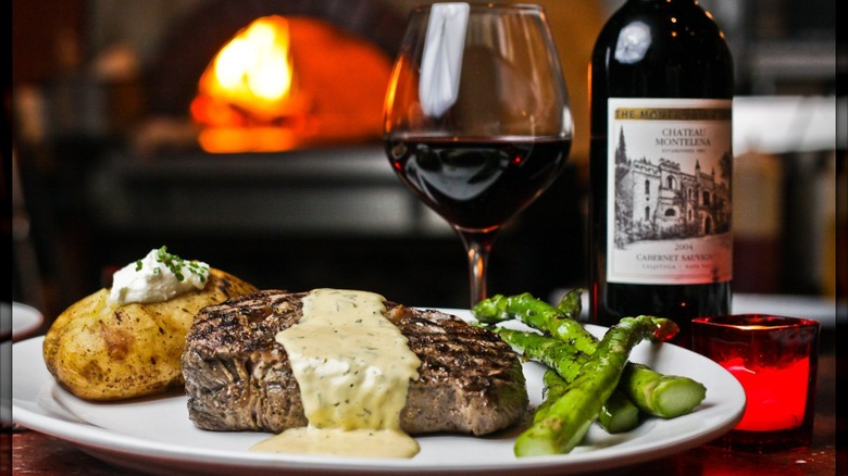 Steak, asparagus, and baked potato with bottle and glass of red wine