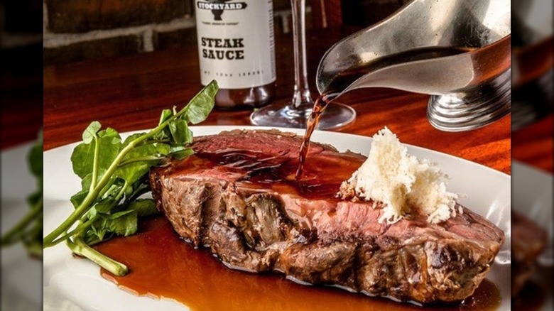 Aus ju being poured over steak on a plate with greens