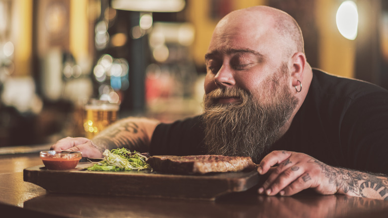 Man sitting at bar smelling the aroma of a steak on wooden board