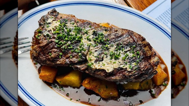 Strip steak on white plate with serving of fried potatoes