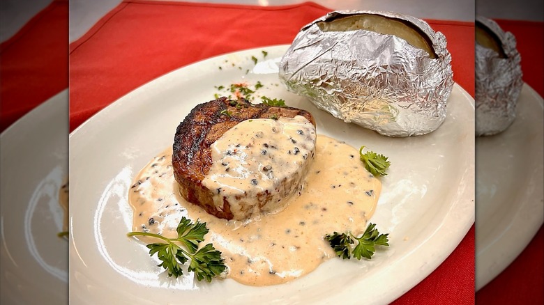 Steak with sauce and a baked potato on plate with red placemat