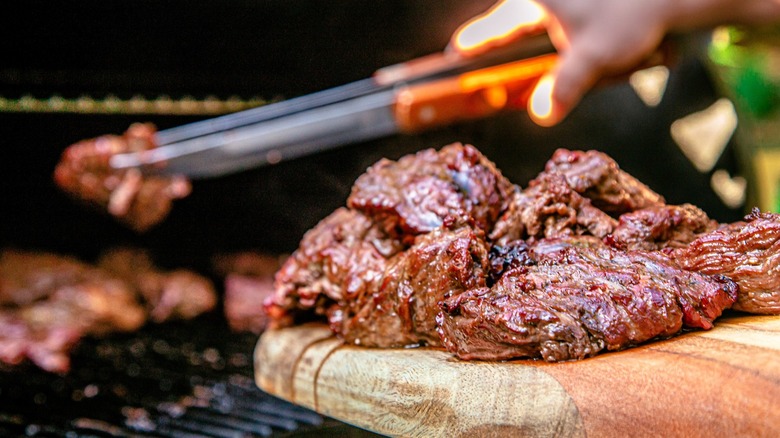 Steak tips on wooden board with more on grilled in blurred background
