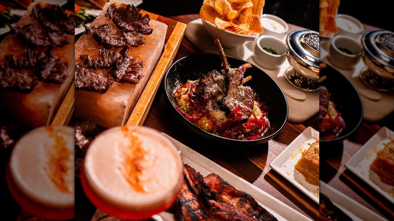 Assortment of steak dishes, cocktails, sides, and dipping sauces on wooden table