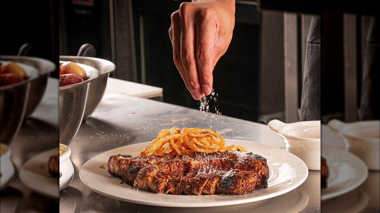 Hand sprinkling salt on a steak on plate in the kitchen