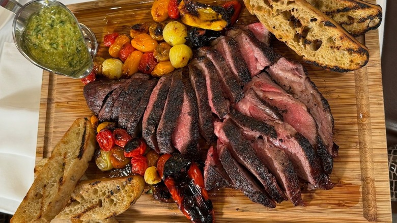 Sliced steak on board with roasted vegetables and bread