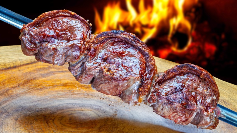 Picanha skewer over wood table with fire in background
