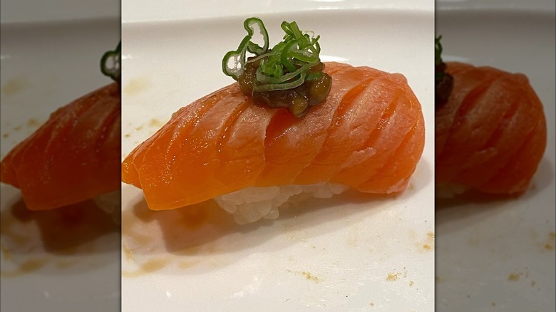Salmom nigiri on a white plate topped with green onion