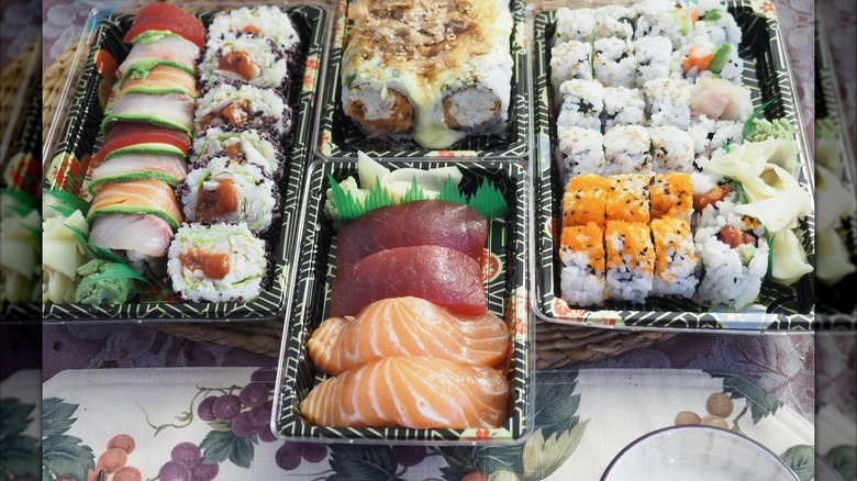 Black to-go containers with assorted nigiri, sashimi, uramaki, and salad