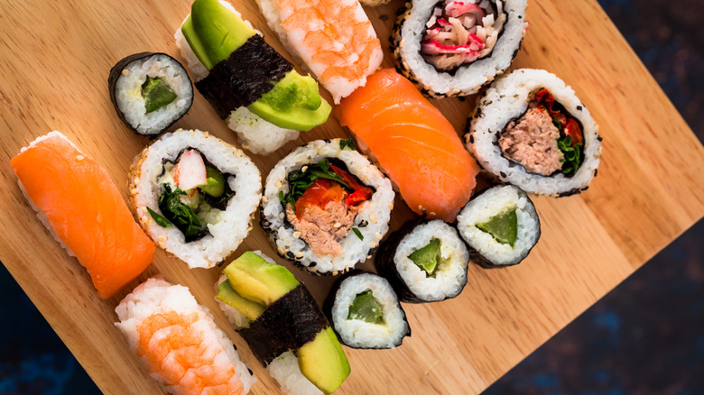 Close up macro color image depicting an arrangement of fresh traditional Japanese sushi rolls topped with smoked salmon, prawn and avocado.