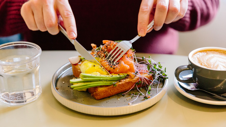 Woman cutting smoked salmon and avocado sandwich