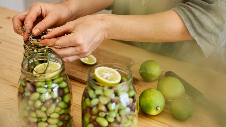 Woman putting herbs and lemons into jars of green olives