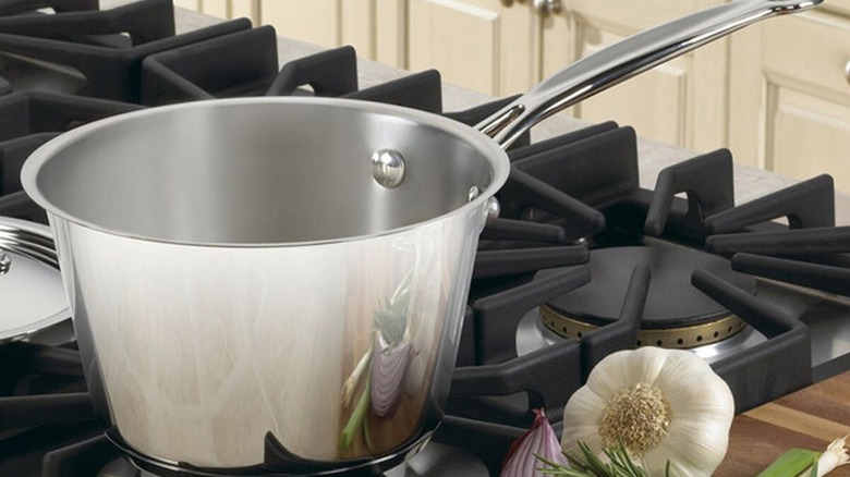 A Cuisinart Windsor pan on a hob next to garlic and onion