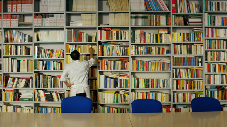 a man in a chefs coat and apron selecting a cookbook in a library