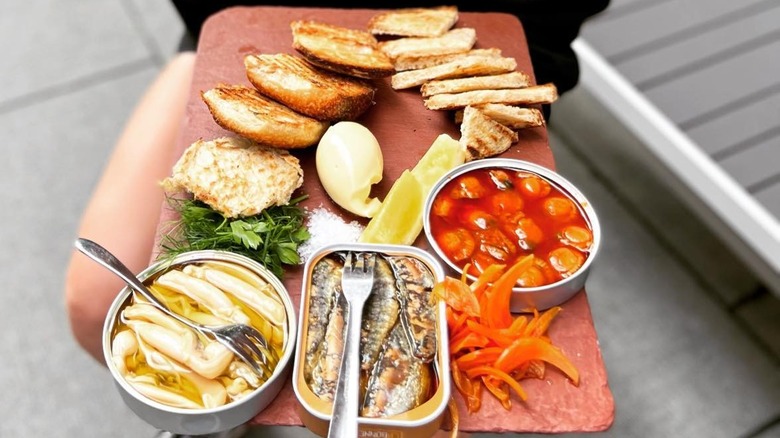 A person holding a tray of tinned fish and bread appetizers at haley.henry