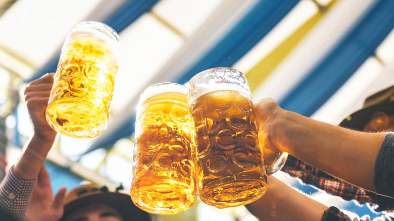 Three people clinking large one-liter steins in a blue and white tent