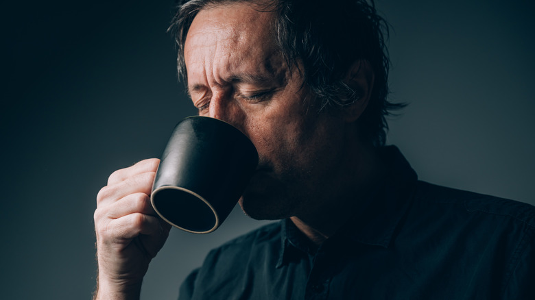 Man in a dark shirt with his eyes closed drinking from a black mug