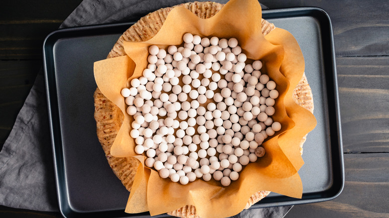 A pie crust covered in parchment paper and filled with pie weights before baking