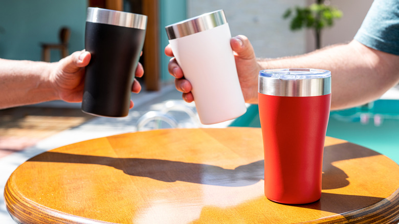 Hands holding tumblers with third tumbler on table