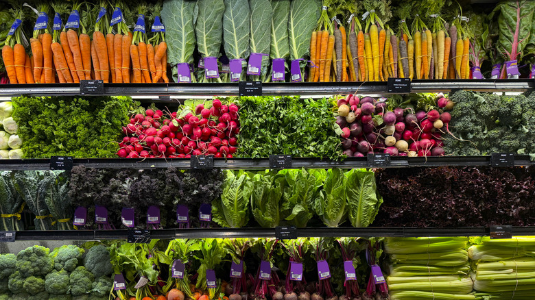 The produce section of a grocery store is shown with vegetables on shelves.