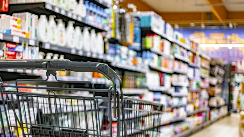 A grey shopping cart is in the shampoo aisle of a grocery store.