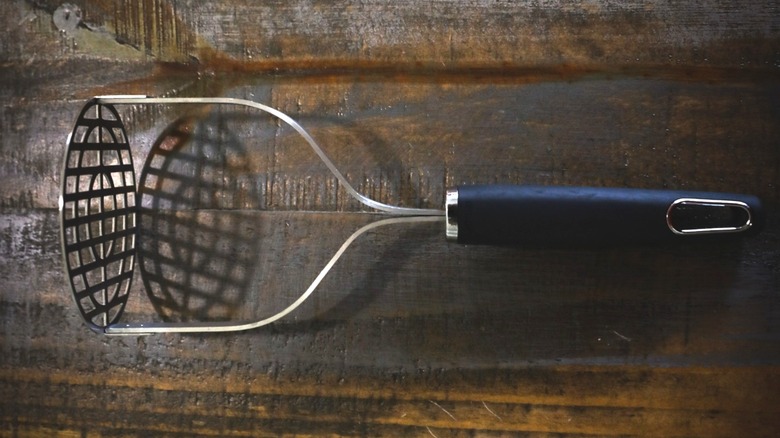 potato masher on dark wooden table