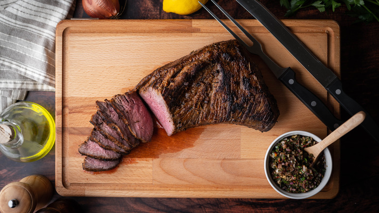 A grilled tri-tip steak on a cutting board with chimichurri