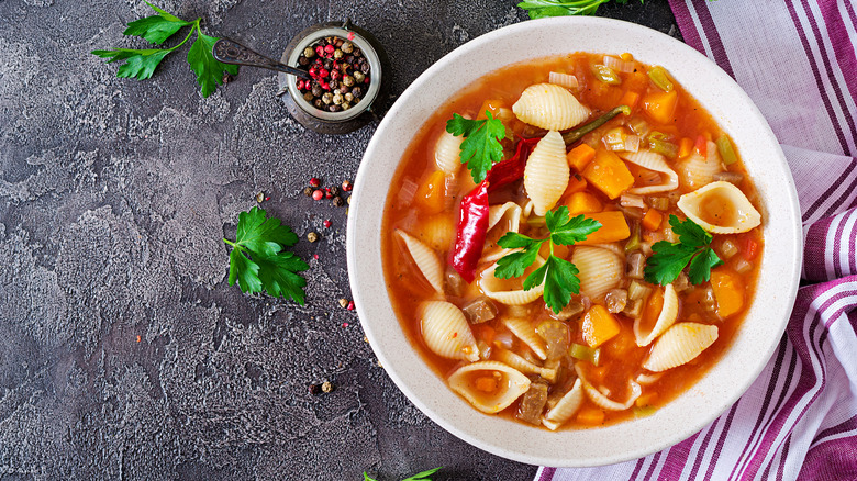 Bowl of vegetable soup with shell pasta, garnished with sprigs of parsley