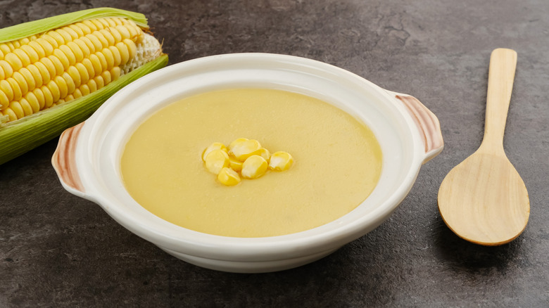 Bowl of corn chowder next to wooden spoon and corn cob