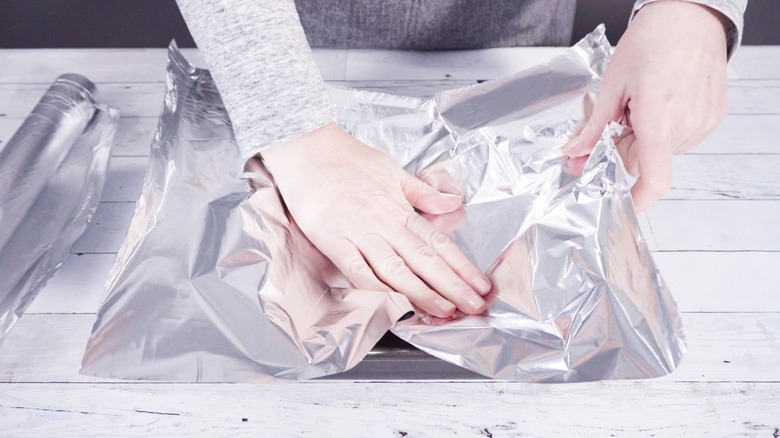 person lining tray with aluminum foil