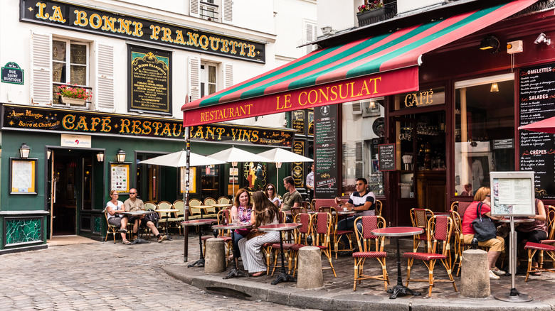The outside of a quaint French cafe with patrons sitting in the outdoor tables and enjoying food and drinks