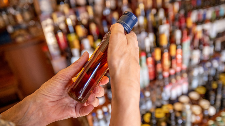 Hands holding a small bottle of brown liquor above a large array of other bottles of different types and sizes