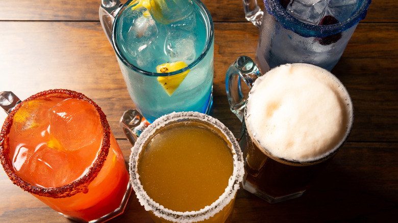 A variety of colorful cocktails sitting on a wooden bar, viewed from above