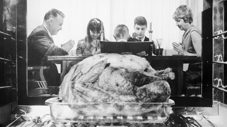 A view of a family praying from inside an oven, a roasting turkey in the foreground