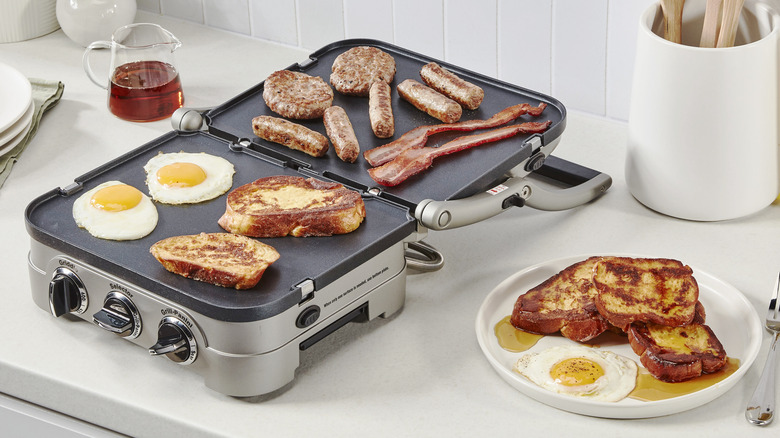 Eggs, sausuage, bacon, and french toast being made on a griddle