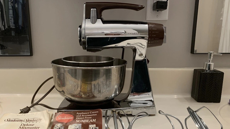 A chrome 1950s Sunbeam Mixmaster on a kitchen counter next to a ceramic cookie container