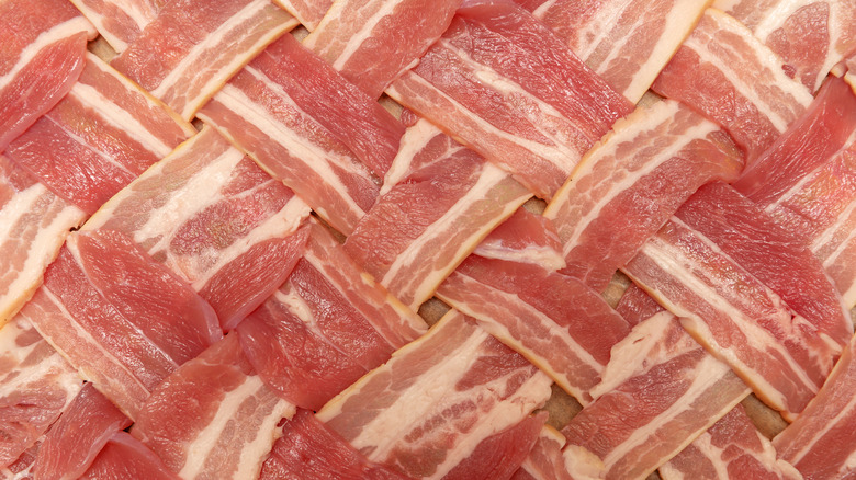 A close-up of strips of raw bacon, woven into a lattice pattern