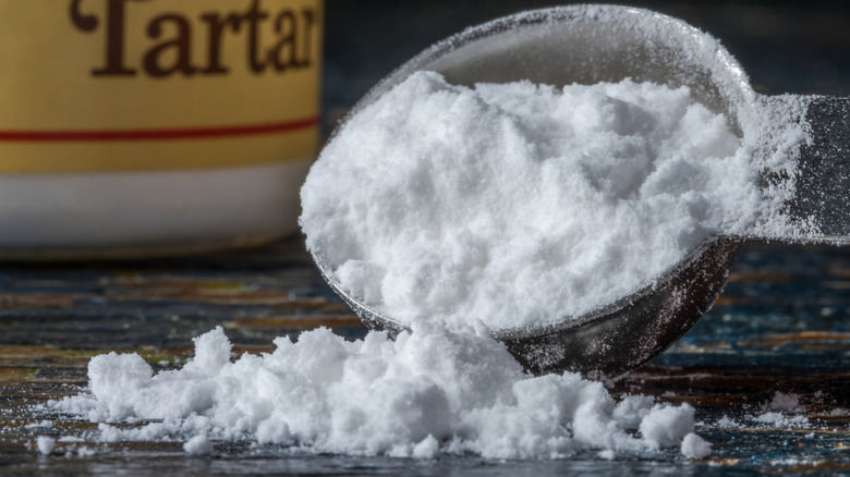 Cream of tartar spilling out of a measuring spoon in front of a cream of tartar container