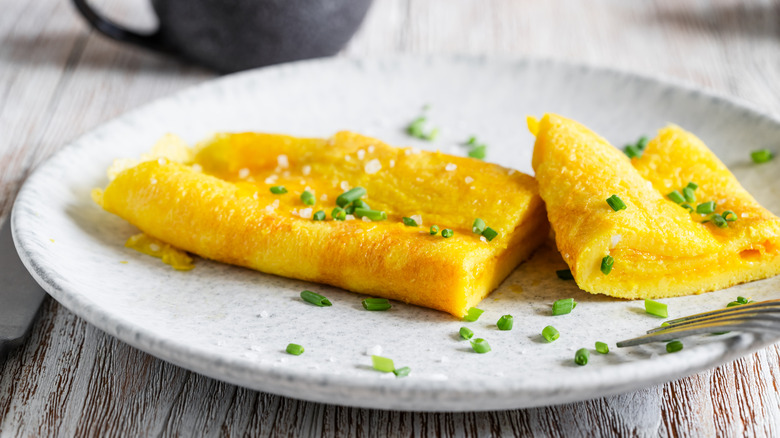 Sliced French omelet on a plate garnished with chives and flaky salt