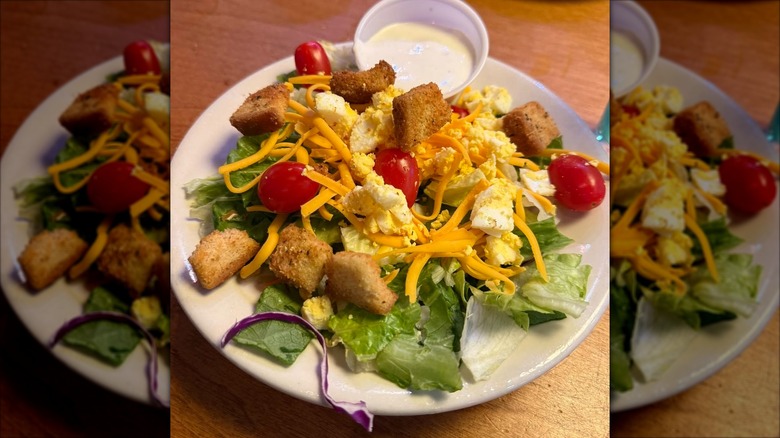 Plate of house salad from Texas Roadhouse with croutons, cheese, and cup of dressing on side