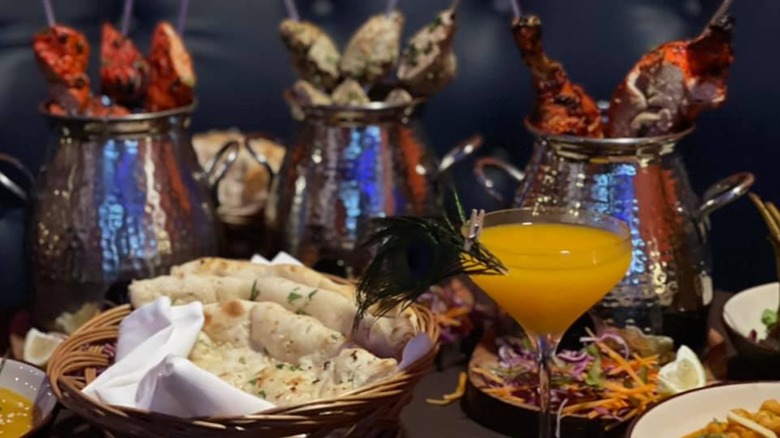 Assortment of Indian dishes including naan and meat skewers with cocktail
