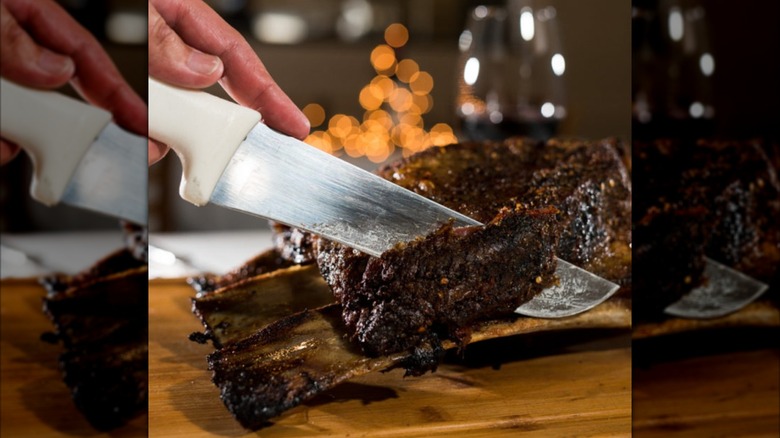 Hand and knife carving a beef rib on wooden surface