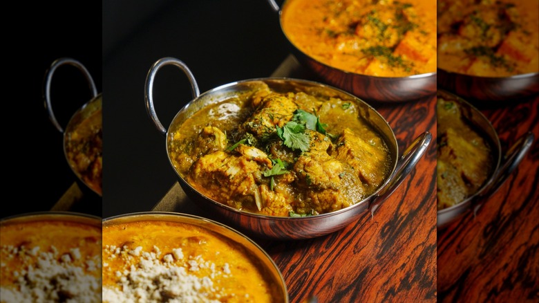 Three Indian dishes in silver bowls on wooden table