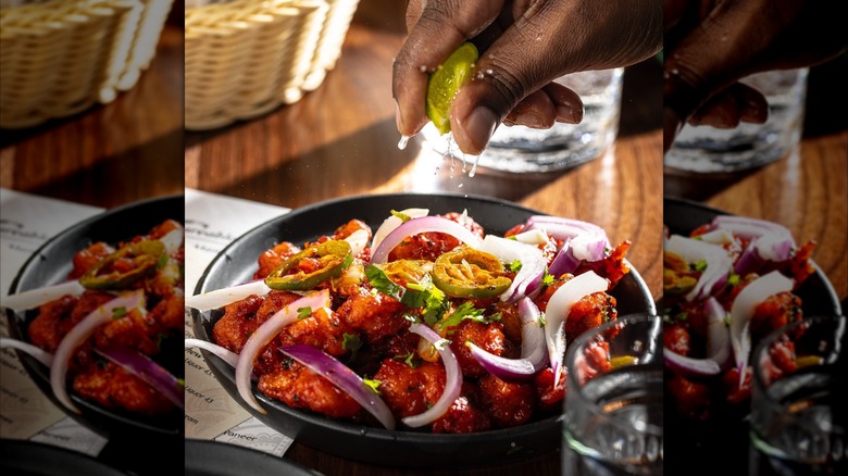 Hand squeezing lime on dish of gobi with onions and cilantro
