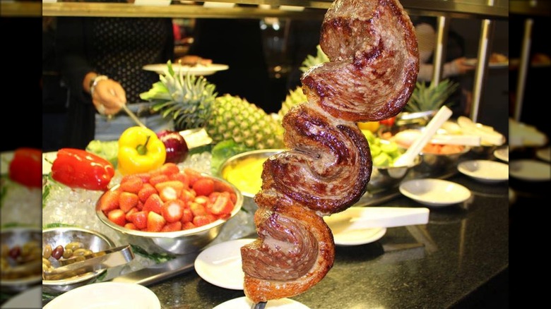 Steak on a skewer in front of buffet table with fruit