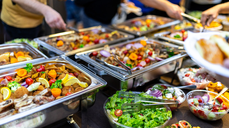 Trays of food on a buffet table with people serving themselves