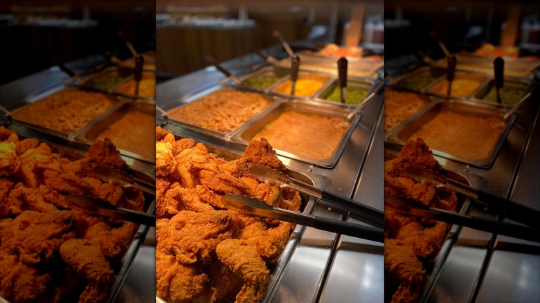 Assrtoemtn of foods on a buffet including fried chicken, gravy, and greens