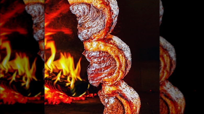 Picanha steaks on a skewer in front of wood fire