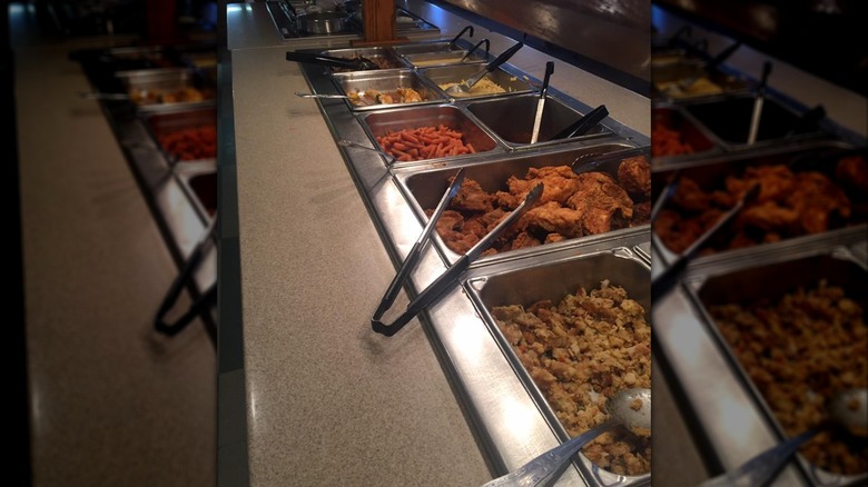 Buffet line with fried chicken, stuffing, carrots, and other trays